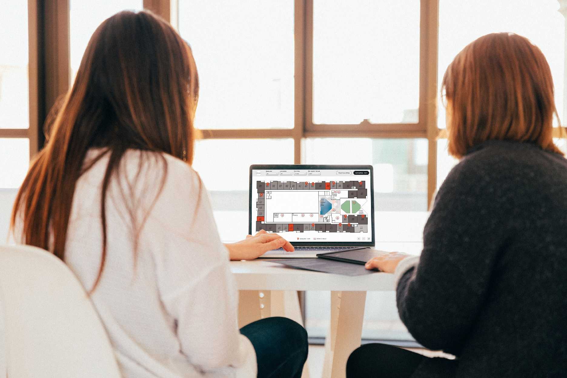 Two women sitting at a table using Pynwheel interactive property website map to search for apartments